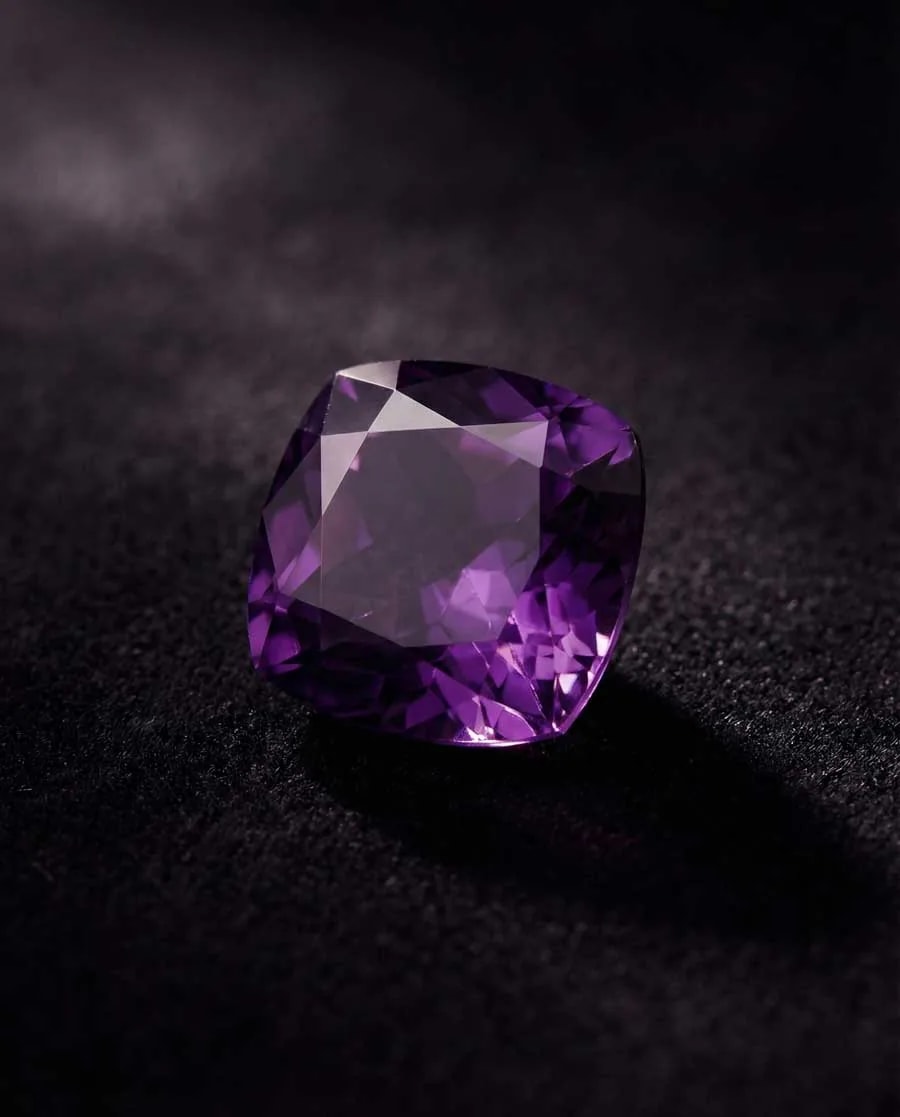 Deep purple faceted amethyst gemstone showcasing rich violet color with subtle red flashes on neutral background