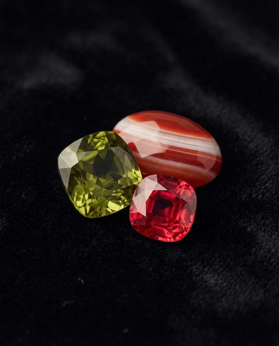 Triptyque horizontal présentant un cristal brut de péridot vert citron, un spinelle rouge vif facetté et un camée de sardonyx à bandes représentant les pierres de naissance d'août