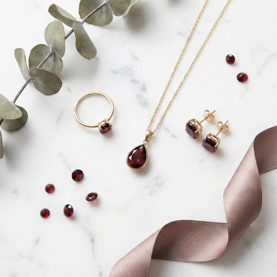 Коллекция гранатовых украшений (кольцо, подвеска, серьги-гвоздики) на белом мраморе