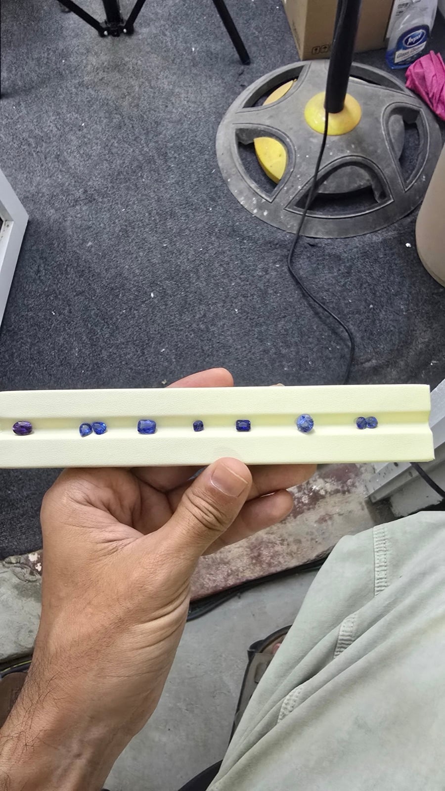 A hand showing a row of rough blue sapphire crystals in a Sri Lankan cutting workshop