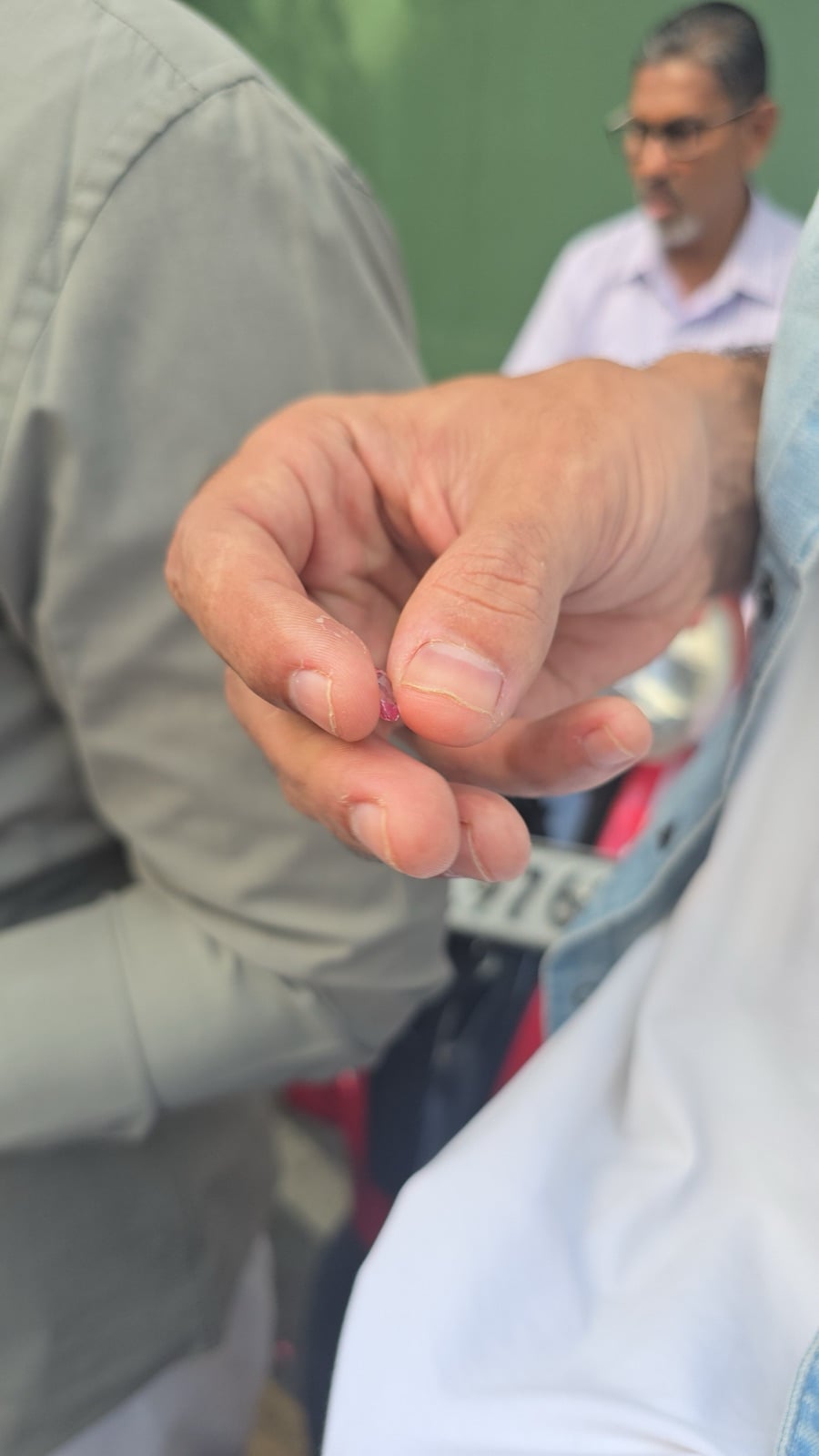 A buyer holding a small loose pink gemstone between two fingers at a gem market in Sri Lanka