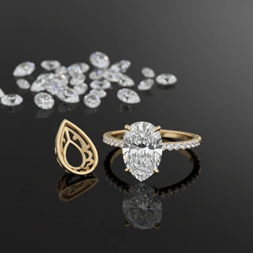 A pear cut diamond in a yellow gold pave solitaire, next to an empty pear shaped gold basket, with loose diamonds scattered behind