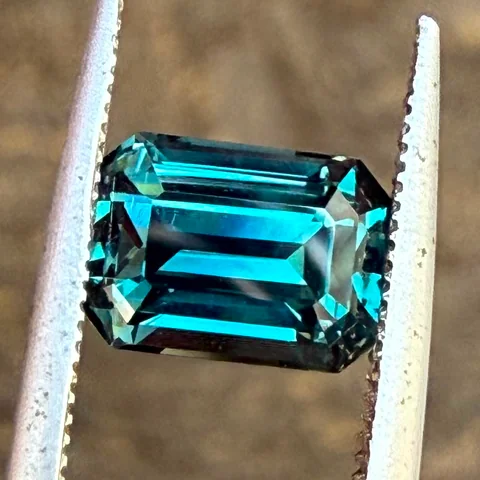 The same teal sapphire held in tweezers outdoors in direct sun