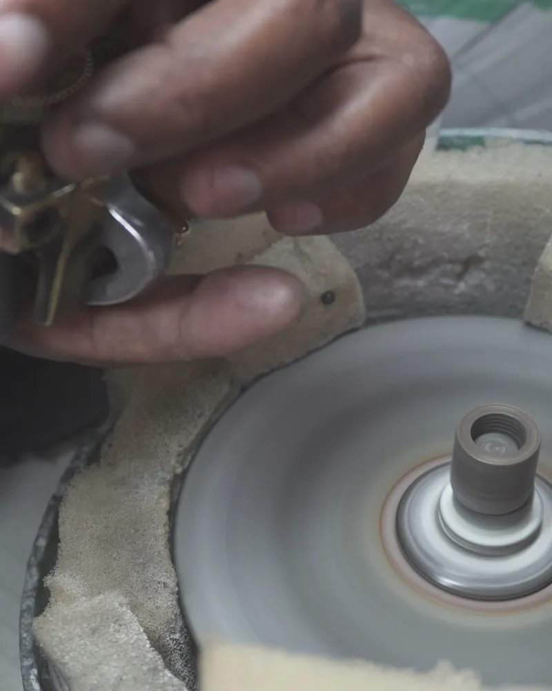 A cutter's hands bring a stone held in a handpiece onto a spinning lap wheel