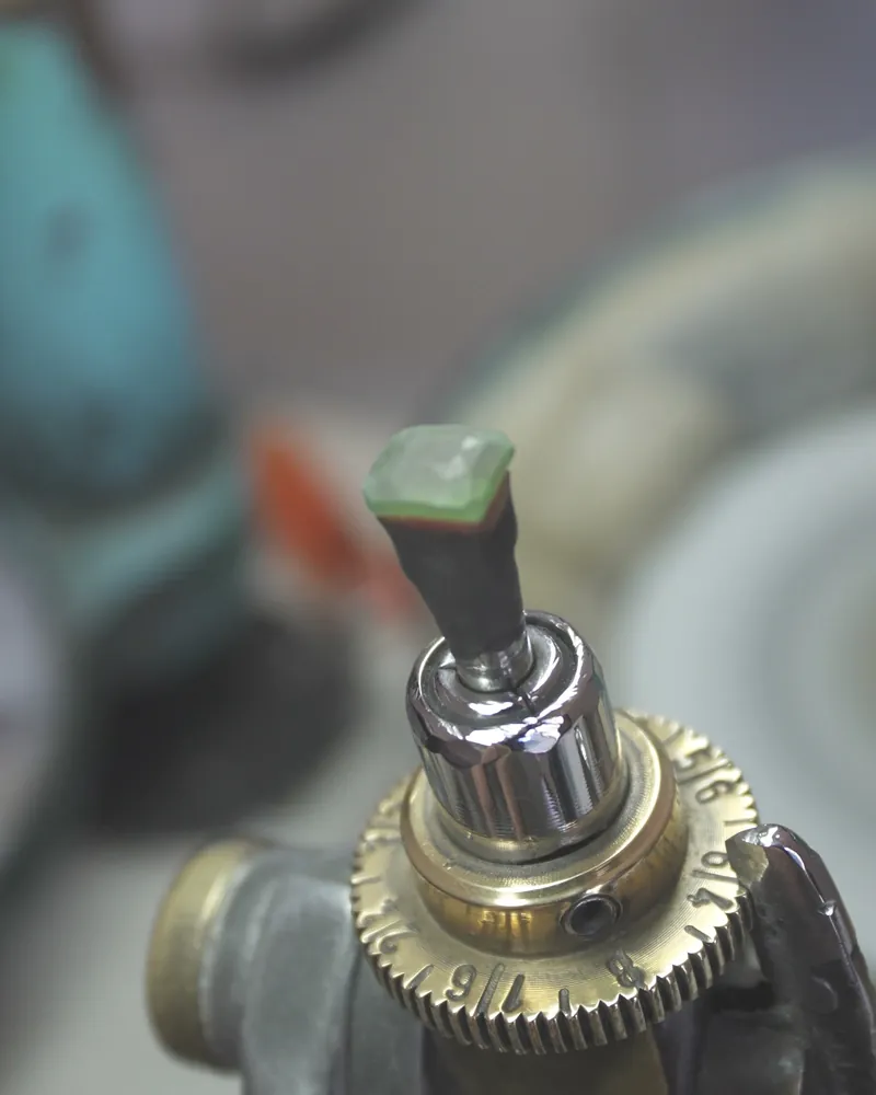 Green tsavorite garnet preform cemented on a dop, mounted on a faceting handpiece with a brass index gear