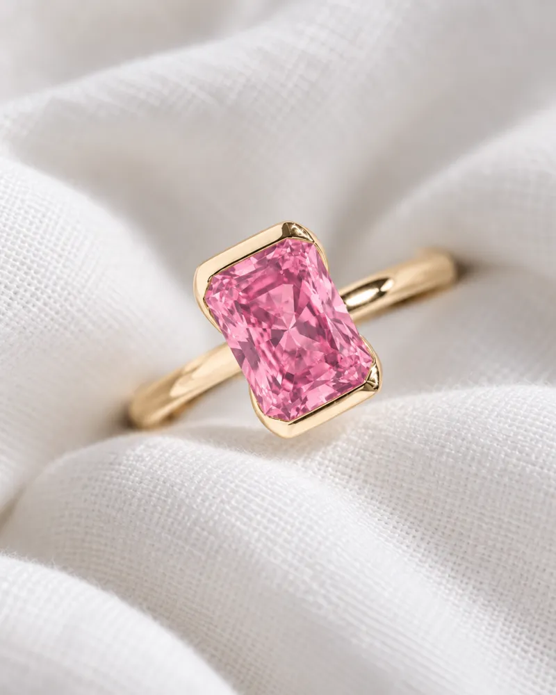 Illustration d’une bague en or avec un spinelle rose taille radiant tenu par le métal sur ses deux petits côtés, posée sur un coton blanc plié.