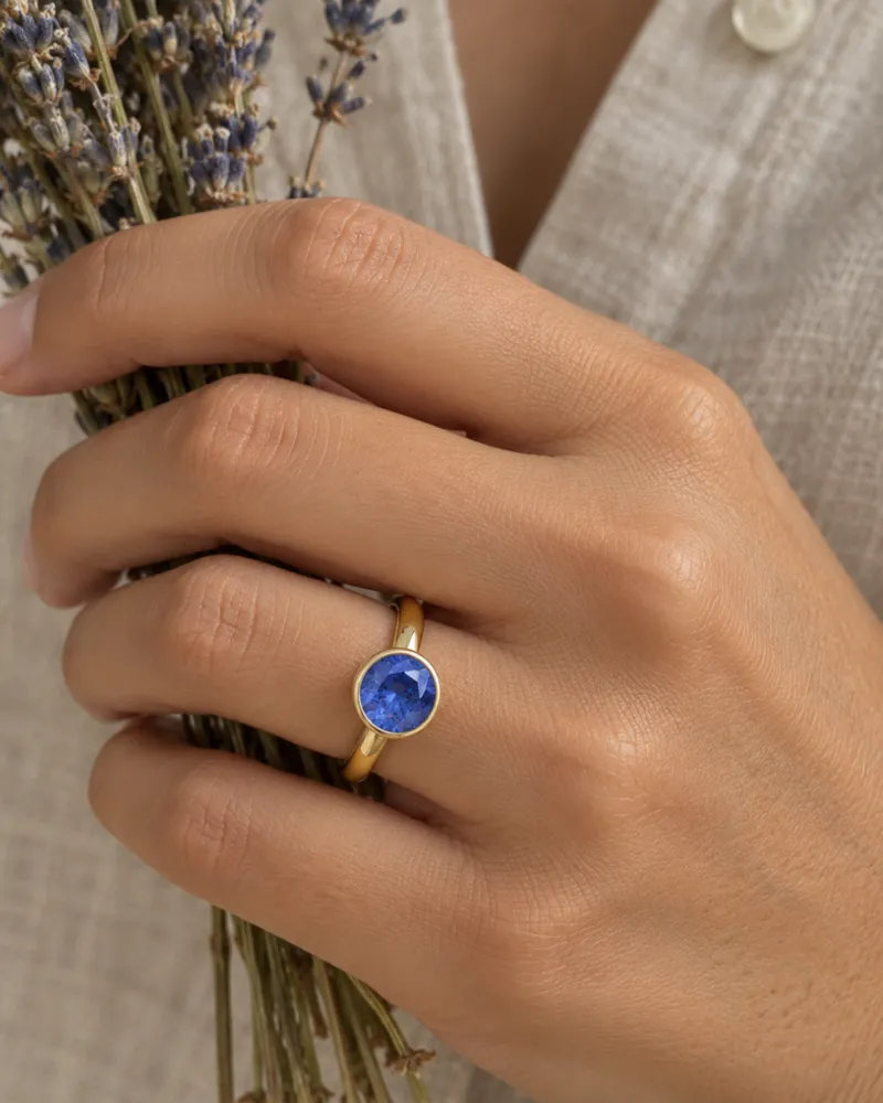 Illustration of a blue sapphire engagement ring, Bezel style, worn on a hand.
