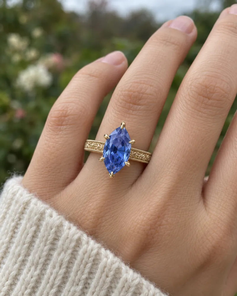 Illustration of a blue sapphire engagement ring, Marquise style, worn on a hand.