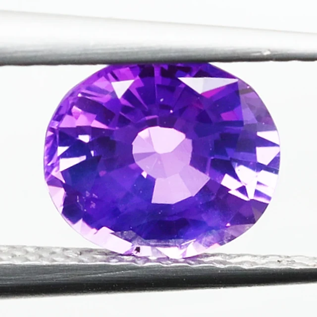 Loose sapphire listed as purple, 1.59 ct, oval cut, held in tweezers on a light grey ground