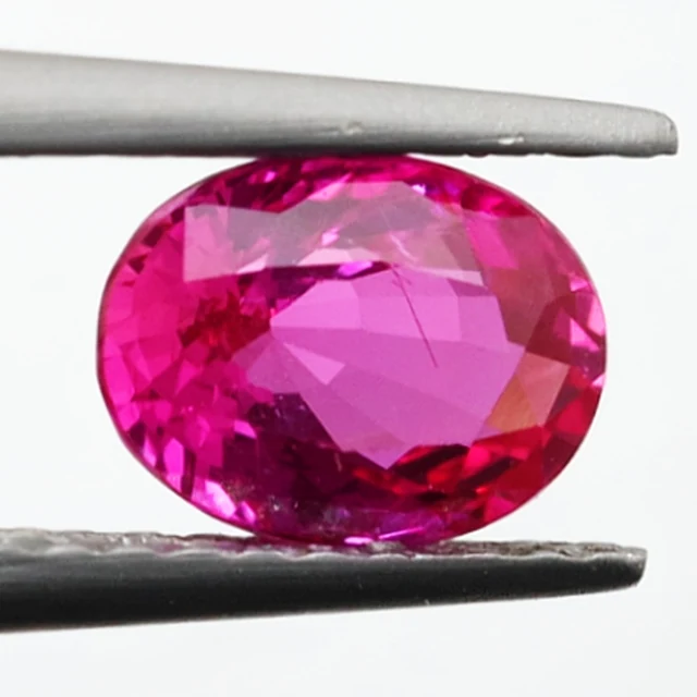 Loose sapphire listed as vivid hot pink, 1.05 ct, oval cut, held in tweezers on a light grey ground