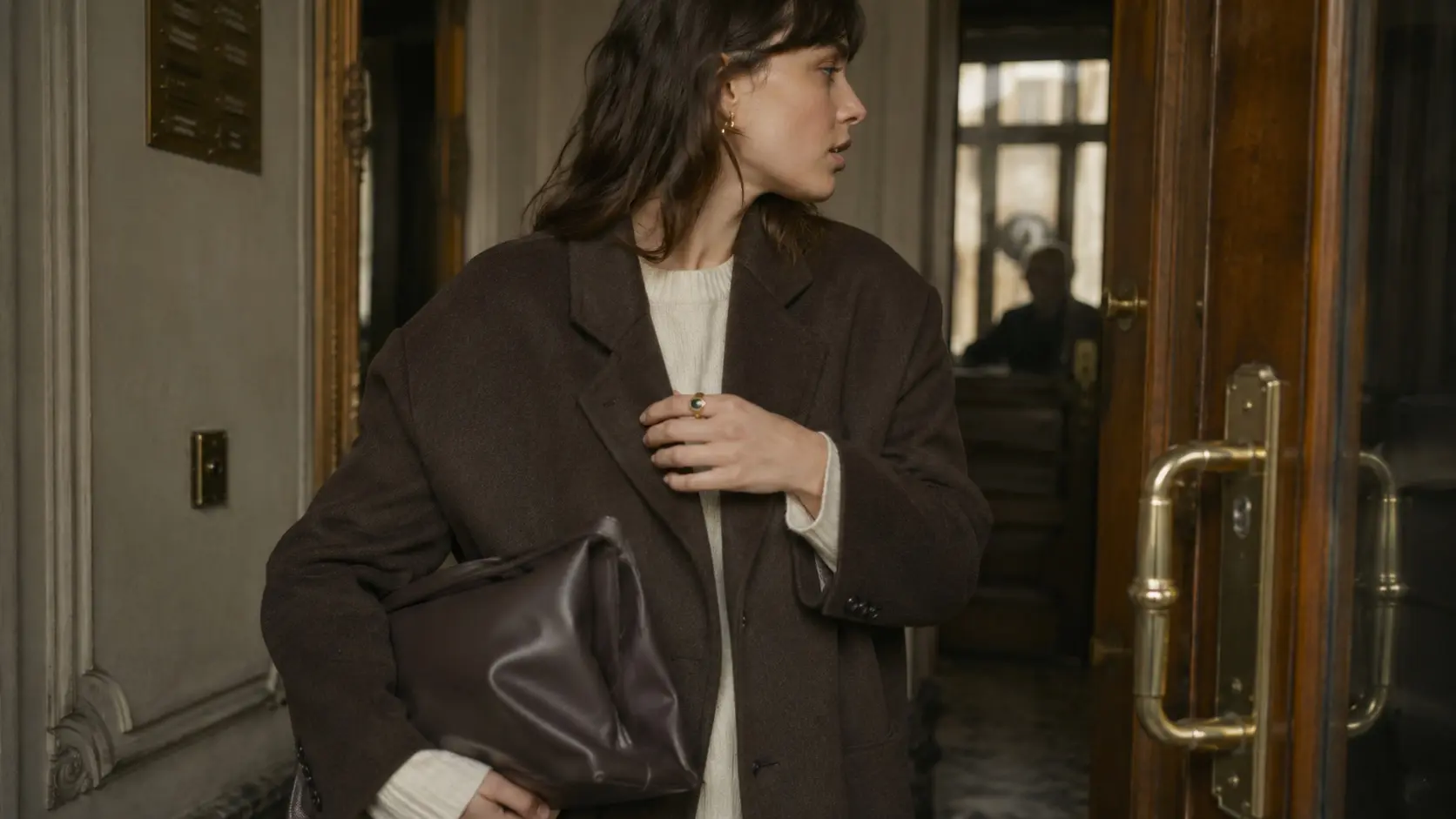 Silhouette in a brown coat in a Parisian building entrance, colored stone ring in hand